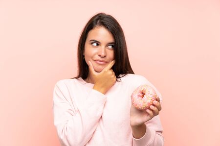 Young girl holding a donut over isolated pink background thinking an ideaの写真素材