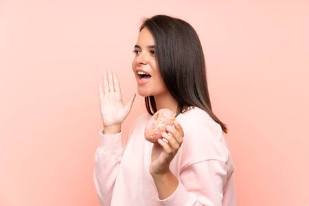 Young girl holding a donut over isolated pink background shouting with mouth wide openの写真素材
