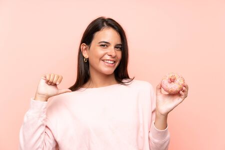 Young girl holding a donut over isolated pink background proud and self-satisfiedの写真素材