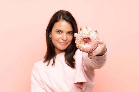 Young girl holding a donut over isolated pink backgroundの写真素材
