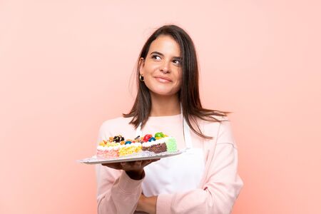 Young girl holding lots of different mini cakes over isolated background looking up while smilingの写真素材