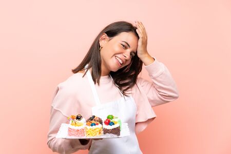 Young girl holding lots of different mini cakes over isolated background has realized something and intending the solutionの写真素材