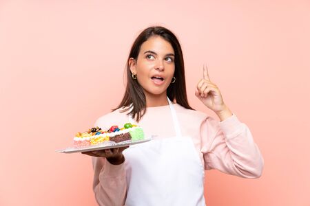 Young girl holding lots of different mini cakes over isolated background intending to realizes the solution while lifting a finger upの写真素材