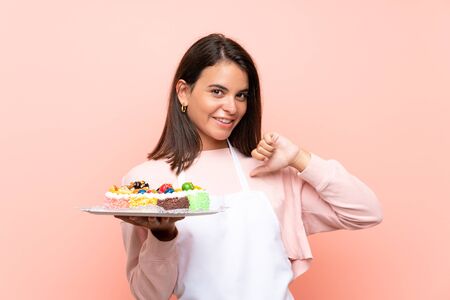 Young girl holding lots of different mini cakes over isolated background proud and self-satisfiedの写真素材