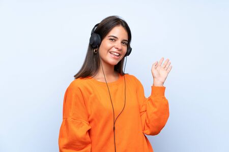 Young woman listening music with a mobile over isolated blue wall saluting with hand with happy expressionの写真素材