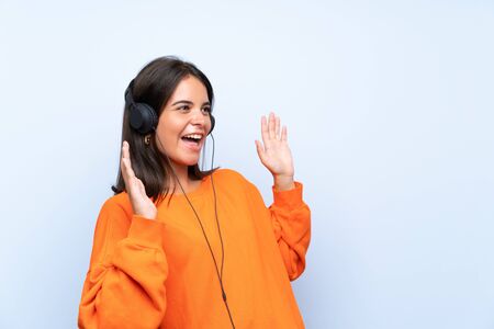 Young woman listening music with a mobile over isolated blue wall with surprise facial expressionの写真素材