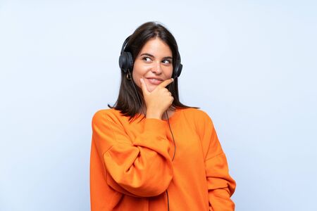 Young woman listening music with a mobile over isolated blue wall thinking an ideaの写真素材