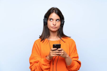 Young woman listening music with a mobile over isolated blue wallの写真素材