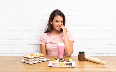 Young girl with lots of different mini cakes nervous and scaredの写真素材