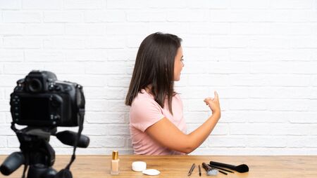 Young girl recording a video tutorial pointing back with the index fingerの写真素材