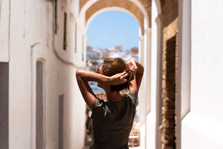 Pretty brunette woman picking up her hair on a white street while traveling. Green dress and sunglasses.の写真素材