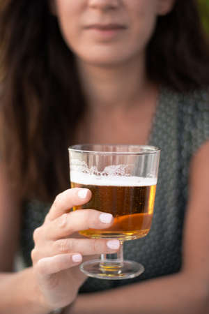 Beautiful brown woman in a green dress holding a glass of beer on a sunny terrace. Selective focus.