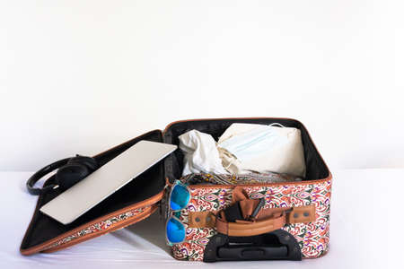 Open suitcase with female clothing, laptop, headphones, sunglasses and face mask. Coronavirus.の写真素材