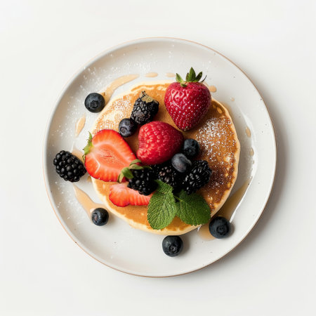 A white plate is presented with a stack of fluffy pancakes generously topped with an assortment of colorful and fresh fruits, including strawberries, blueberries, and bananas. The pancakes are drizzled with golden maple syrup, creating a visually appealing and appetizing breakfast or brunch dish.の素材