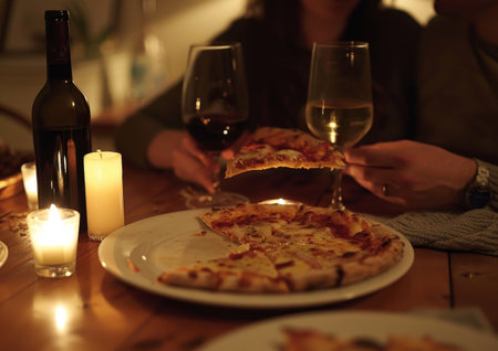 A group of people gathered around a table, enjoying slices of pizza, and sipping on glasses of wine. The group is engaged in lively conversation and laughter.の素材
