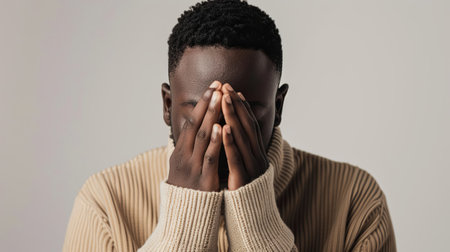 A man sitting with hands covering his face, displaying emotions of distress, sadness, or fatigue.の素材