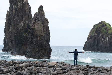 Man with arms wide open looking at Ribeira da Janela islet in Madeiraの写真素材