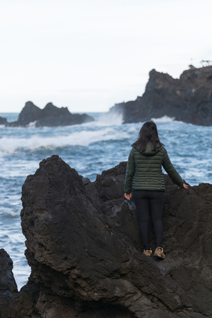Woman seeing waves crashing on a rocky beach at Seixal, Madeiraの写真素材