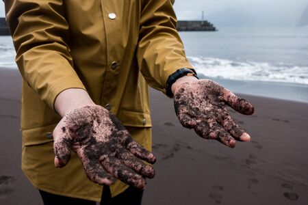 Woman on a yellow jacket at a black sand beach showing her handsの写真素材