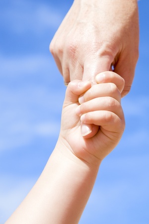 Adult holding a child by the hand against a cloudy blue skyの写真素材