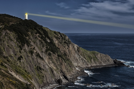 Lighting lighthouse at dusk, shining from the top of a cliffの写真素材
