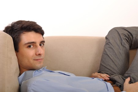 smiling attractive young man lying on the couchの写真素材