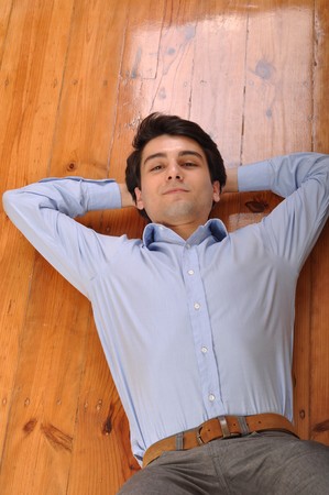 smiling attractive young man lying on wooden floor at homeの写真素材