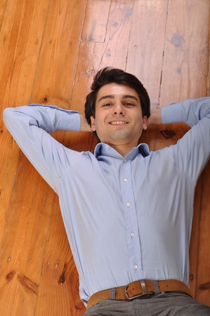 smiling attractive young man lying on wooden floor at homeの写真素材
