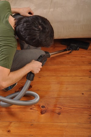 back view of a young man with vacuum cleaner doing the houseworkの写真素材