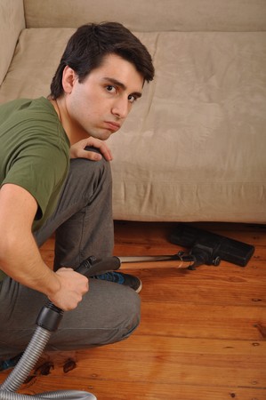 exhausted young man with vacuum cleaner doing the houseworkの写真素材