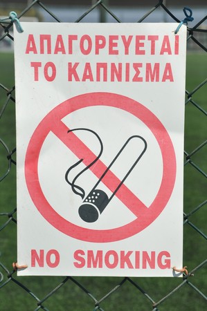 forbidden to smoke sign hanging on a sports court fence (greek and english language)の写真素材