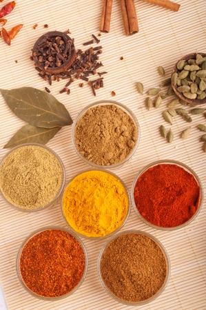gorgeous setting with cooking spices and herbs (bay leaves, cumin, coriander, chili powder, cloves, cardamom pods, cinnamon sticks, paprika, piri piri, turmeric) on a wooden matの写真素材