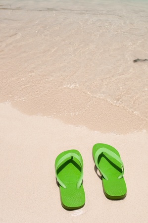green flip flops on the beach (copy-space available)の写真素材