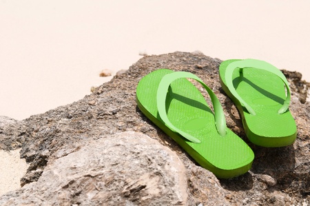green flip flops on a rock at the beach (copy-space available)の写真素材