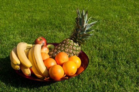 fruit bowl with apples, bananas, oranges and pineapple on the grass fieldの写真素材