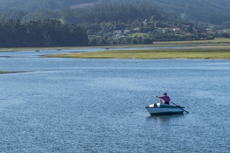ORTIGUEIRA, SPAIN - SEPTEMBER 28, 2019: A man in the sea fishing from his boat.. A sunny day in late summer on the estuary of Ortigueiraのeditorial素材