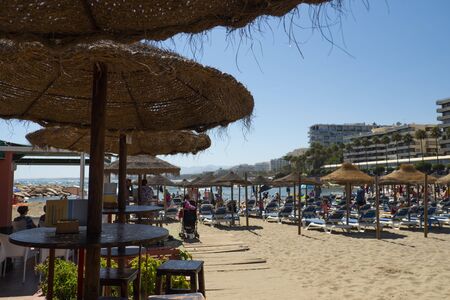 MARBELLA, SPAIN - JUNE 21, 2019: Playa del Faro in Marbella, Malaga, Spain- View of the beach, umbrellas and people on the sand with the boardwalk buildings in the backgroundのeditorial素材
