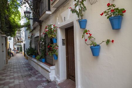 MARBELLA, SPAIN - JUNE 21, 2019: Picturesque street of the historic center of Marbella, Spain. Narrow alley full of blue pots, plants and flowersのeditorial素材