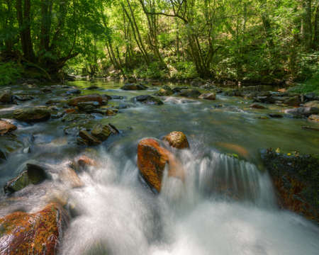 River flows between orange boulders and green oak and birch forests in Courel Mountain Range geoparkの写真素材