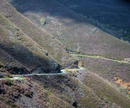 Mountain road winding between heather-covered slopes, in the Mountains of Courel geopark