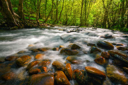 Reddish boulders in the stream of a river in Ancares Mountain Range in Cervantes Lugo Galicia