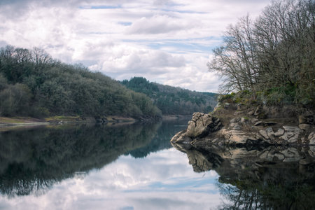 Fractured granite rocks are reflected in the calm waters of the Minho river near Lugo Galiciaの写真素材