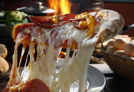 Hot pizza slice with melting cheese with wood oven in background.の写真素材