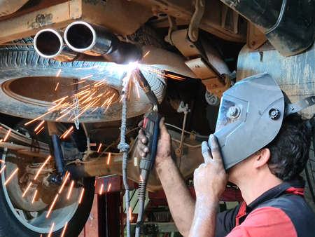Mechanic or welder is fixing a car exhaust system by welding the exhaust pipe