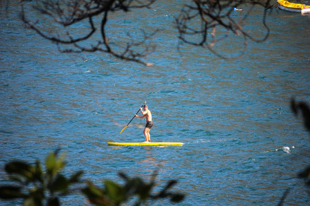 Rio de Janeiro, Brazil, 12 September, 2016: Practicing Stand Up Paddle - SUP seen framed by the branches of a tree in Red Beach. Spring is approaching and the weather in Rio de Janeiro starts to get warmer. On a sunny and hot afternoon people get excited のeditorial素材