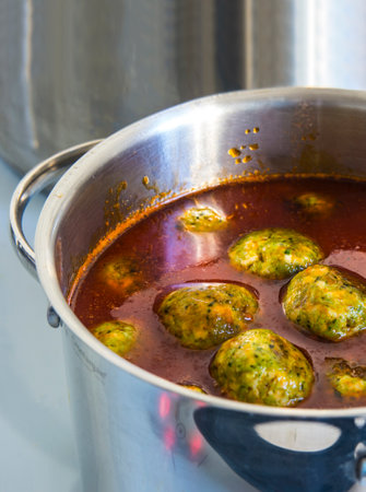 A savory dish of meatball soup simmering on a stovetop, filled with flavorful ingredients and liquids. A delicious recipe cooking in a pot on the stoveの写真素材