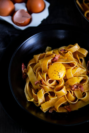 A dish of lasagnette pasta with eggs and bacon served al dente on a table. This recipe combines staple food ingredients to create a delicious Italian cuisine dishの写真素材