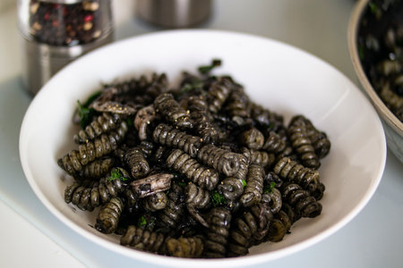 A white plate showcasing an exotic dish of black pasta made from insect larvae. This innovative...