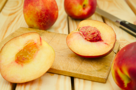 Fresh, vegetarian, juicy red and yellow sliced and whole nectarines on a cutting board with the knife in the backgroundの写真素材