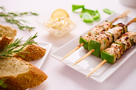 Barbeque Grilled chicken and peppers on skewer served on rectangular plate in restaurant setting with Macedoine dipping sauce and bread.の写真素材